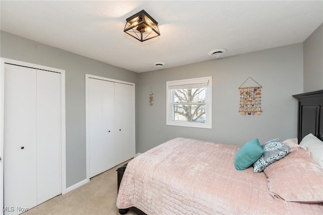 bedroom with visible vents, light colored carpet, and two closets