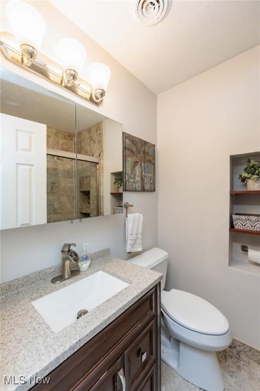 full bath featuring vanity, toilet, visible vents, and a stall shower