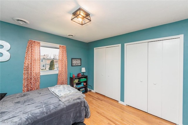 bedroom with visible vents, two closets, and wood finished floors