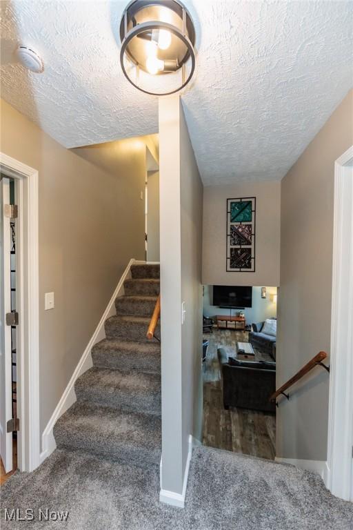 stairway featuring carpet, baseboards, and a textured ceiling