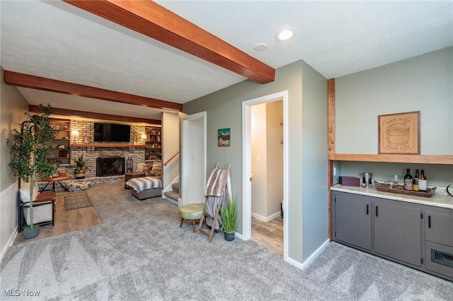 living area featuring stairway, baseboards, a brick fireplace, beamed ceiling, and carpet flooring