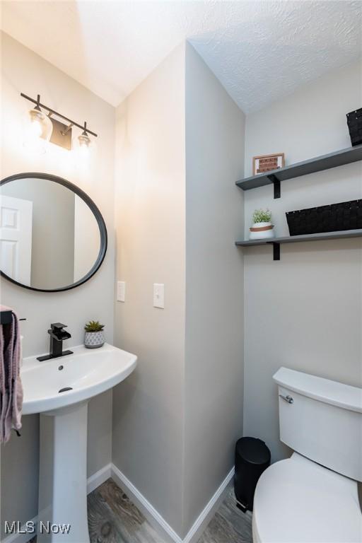 half bathroom featuring a textured ceiling, toilet, baseboards, and wood finished floors