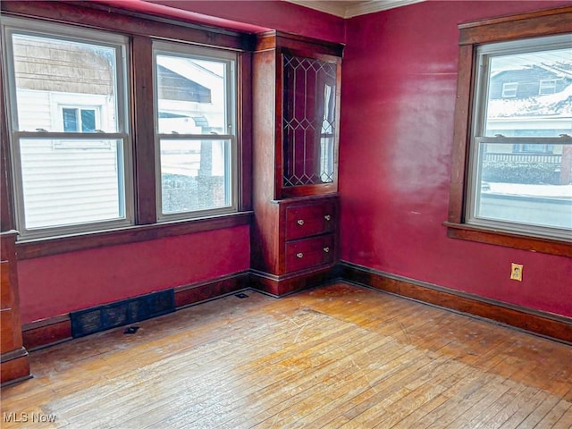 empty room featuring visible vents, baseboards, and wood-type flooring