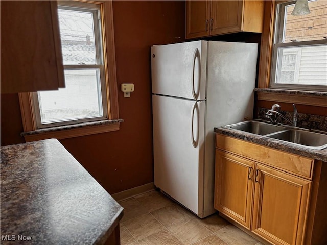 kitchen featuring brown cabinetry, baseboards, freestanding refrigerator, a sink, and dark countertops