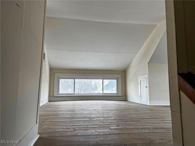 unfurnished living room featuring hardwood / wood-style floors, lofted ceiling, and baseboards