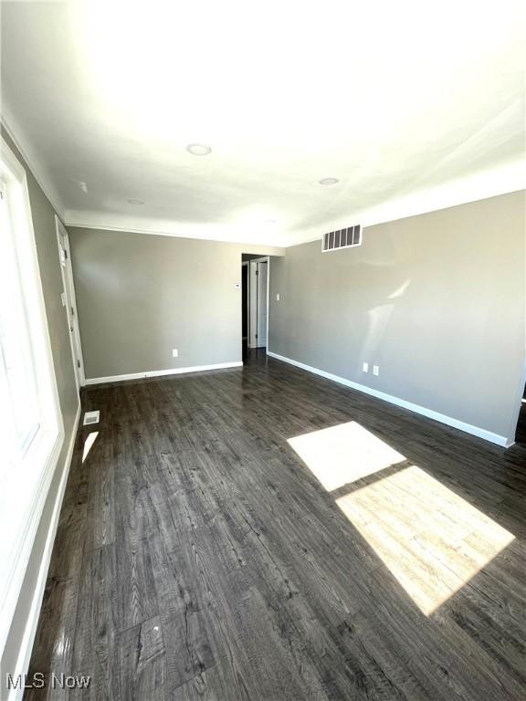 spare room with dark wood-style floors, visible vents, and baseboards