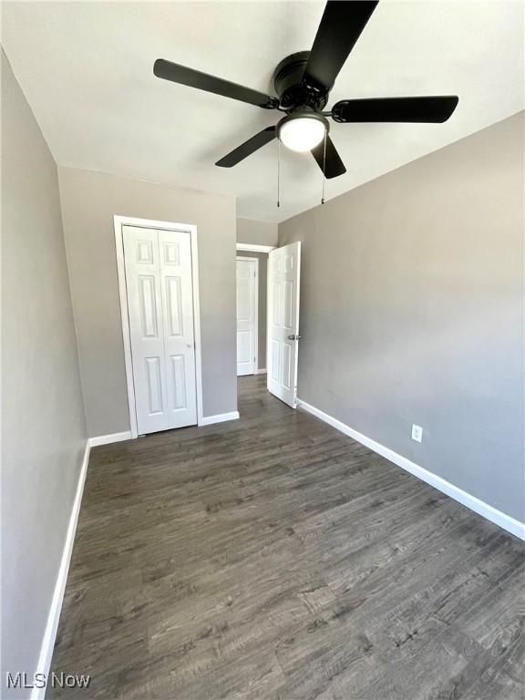 unfurnished bedroom with dark wood-style floors, ceiling fan, a closet, and baseboards