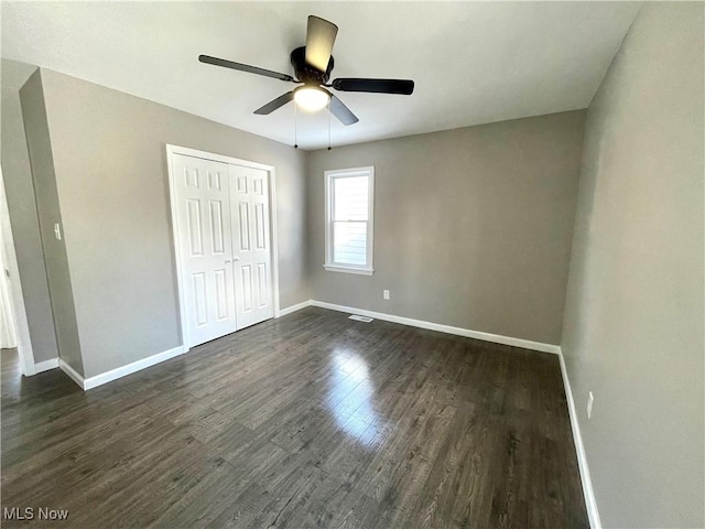 unfurnished bedroom featuring a closet, baseboards, ceiling fan, and dark wood-style flooring