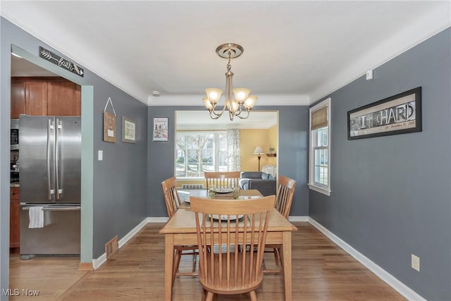 dining space with light wood finished floors, baseboards, and an inviting chandelier