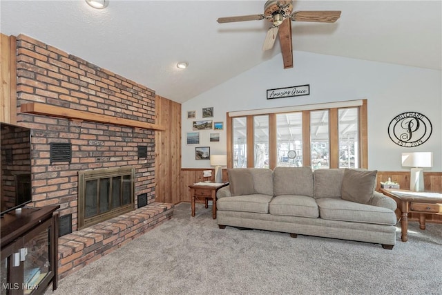 carpeted living area with wooden walls, a wainscoted wall, vaulted ceiling with beams, a fireplace, and ceiling fan