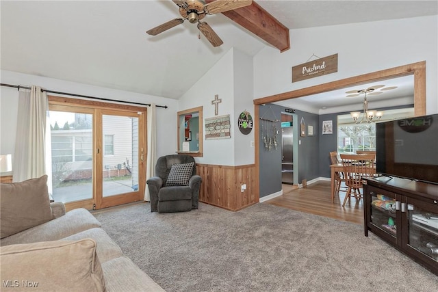 living area with a wainscoted wall, wood walls, lofted ceiling with beams, carpet flooring, and ceiling fan with notable chandelier