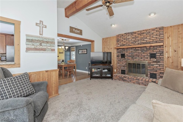 living room with wooden walls, a ceiling fan, beamed ceiling, carpet floors, and a brick fireplace