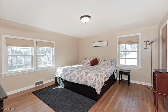 bedroom with hardwood / wood-style floors, lofted ceiling, baseboards, and visible vents