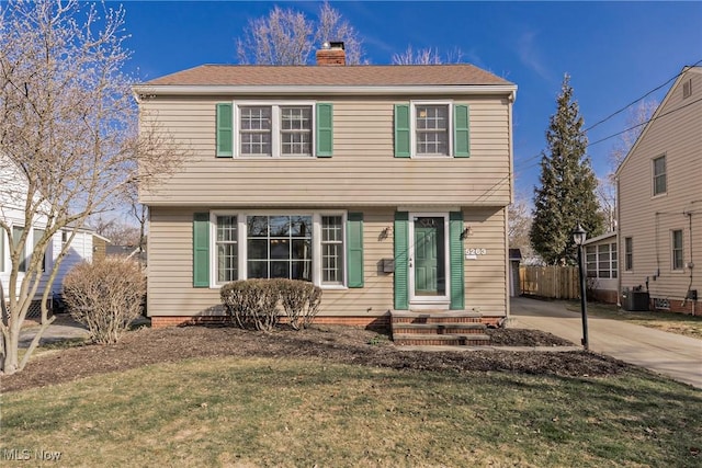 colonial-style house with a front lawn, central AC, fence, concrete driveway, and a chimney