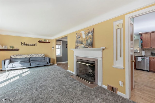 living area with light colored carpet, a fireplace with flush hearth, baseboards, and visible vents