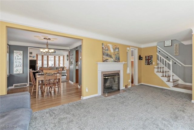 living room with stairway, baseboards, an inviting chandelier, a glass covered fireplace, and carpet flooring