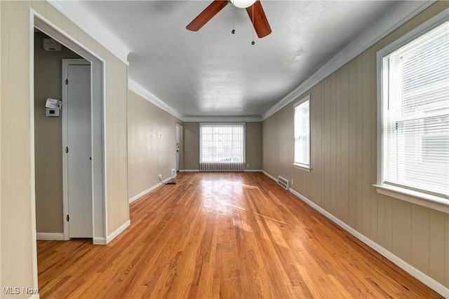 empty room with a ceiling fan, radiator heating unit, light wood-style floors, crown molding, and baseboards