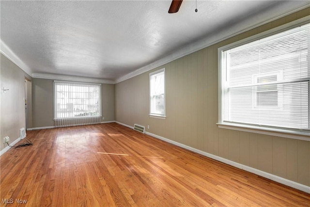 unfurnished room with a wealth of natural light, visible vents, baseboards, and wood finished floors