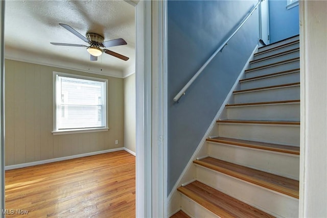 stairs featuring wood finished floors, baseboards, ornamental molding, ceiling fan, and a textured ceiling