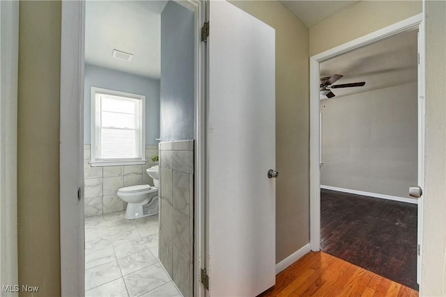 hall with a wainscoted wall, tile walls, visible vents, and light wood-type flooring