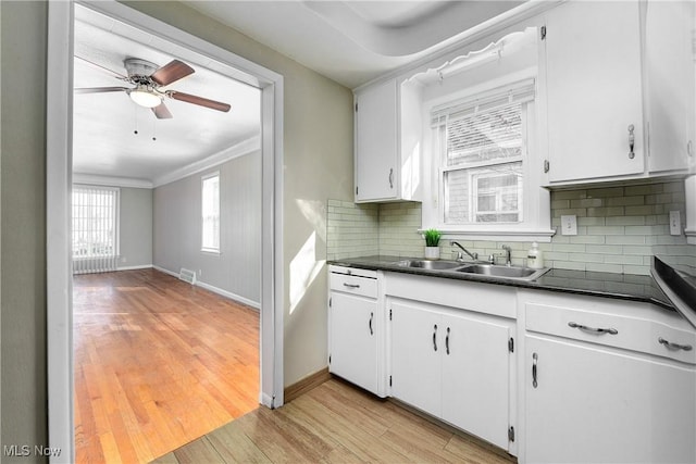 kitchen with dark countertops, white cabinets, light wood-style floors, and a sink