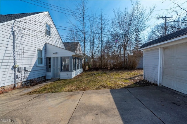 view of home's exterior with driveway, a yard, a garage, and a sunroom