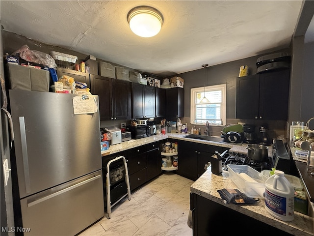 kitchen with a sink, dark cabinetry, light countertops, and freestanding refrigerator