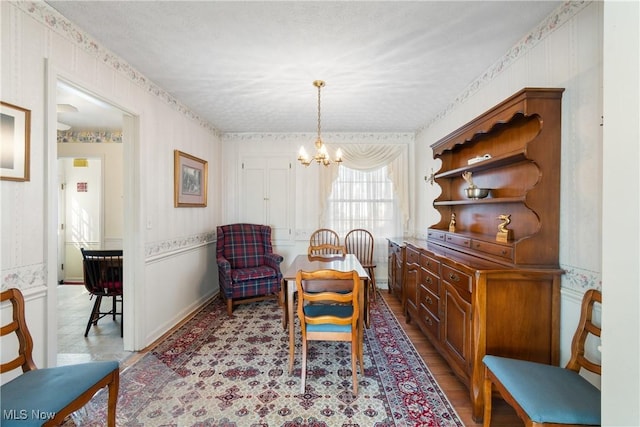 sitting room featuring a textured ceiling, wallpapered walls, light wood-type flooring, and an inviting chandelier