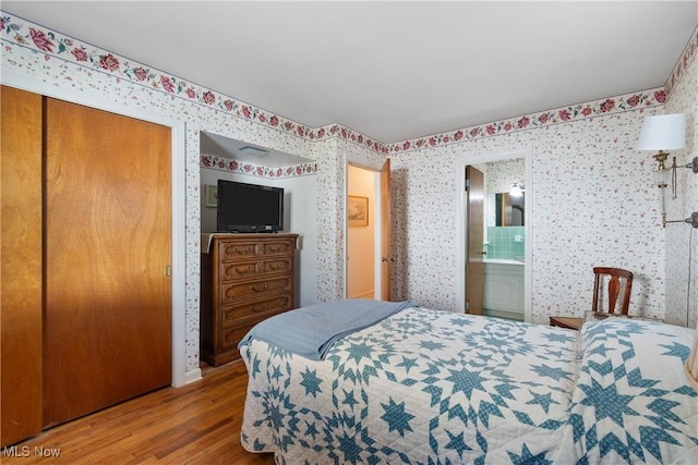 bedroom featuring connected bathroom, wallpapered walls, and wood finished floors