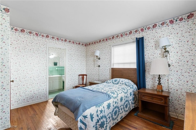 bedroom featuring wallpapered walls, wood finished floors, baseboards, and connected bathroom