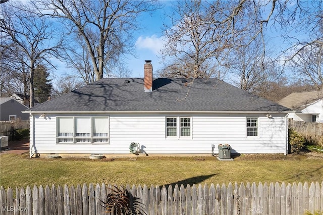 rear view of house featuring a chimney, a lawn, a shingled roof, and fence