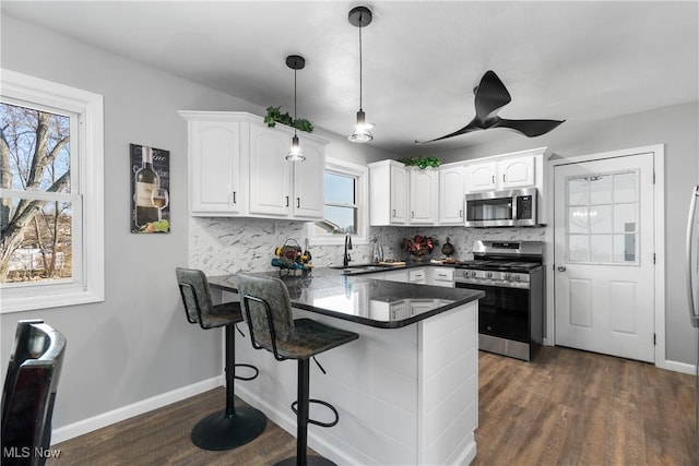 kitchen with a sink, stainless steel appliances, a peninsula, white cabinets, and decorative backsplash