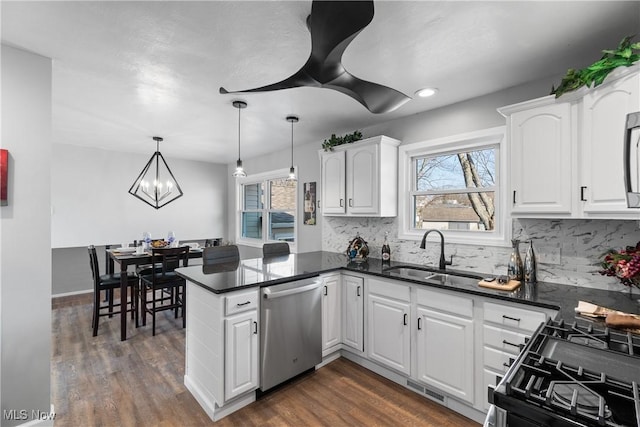 kitchen featuring dark wood finished floors, decorative backsplash, appliances with stainless steel finishes, a peninsula, and white cabinetry