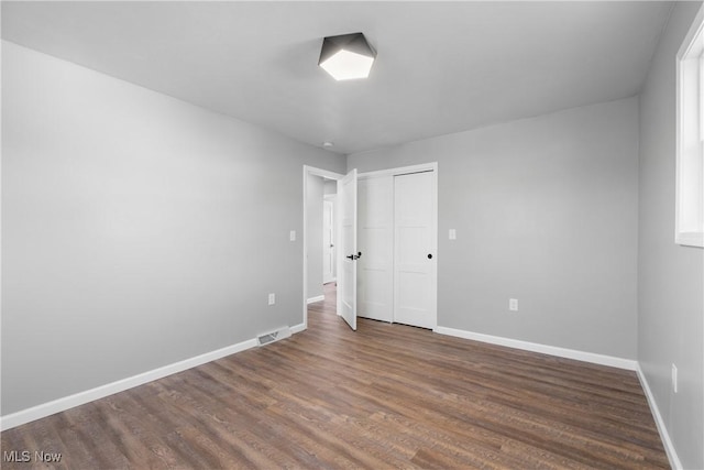 unfurnished bedroom featuring visible vents, baseboards, dark wood-type flooring, and a closet