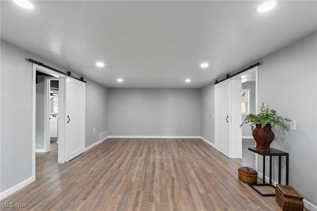 basement featuring recessed lighting, a barn door, and wood finished floors