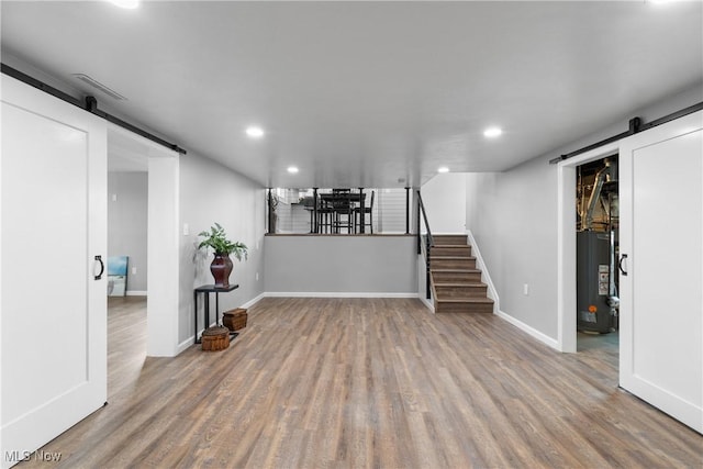 finished below grade area featuring stairs, a barn door, wood finished floors, and water heater