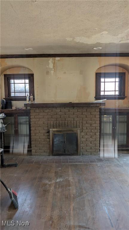 unfurnished living room with hardwood / wood-style floors, crown molding, a brick fireplace, and a textured ceiling