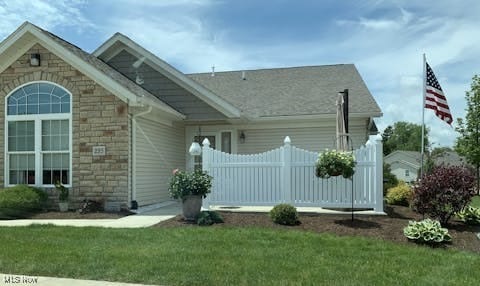 view of front of house with stone siding, a front yard, and fence