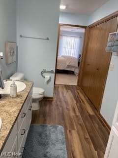 full bathroom with toilet, double vanity, ensuite bathroom, wood finished floors, and a sink