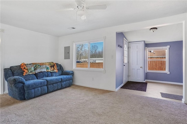 carpeted living room with electric panel, baseboards, visible vents, and ceiling fan