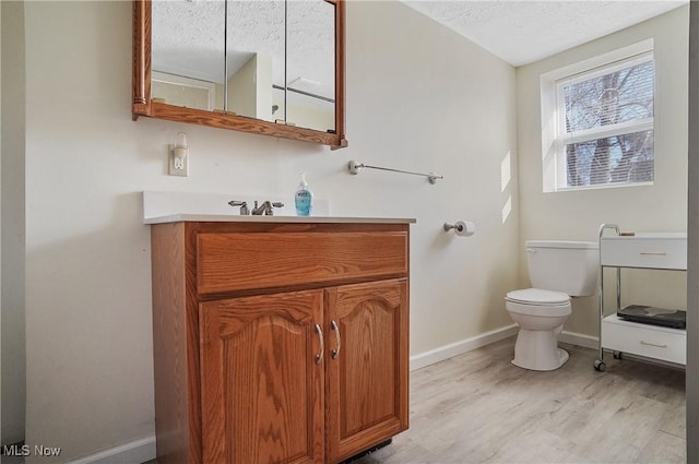 bathroom with toilet, a textured ceiling, wood finished floors, baseboards, and vanity