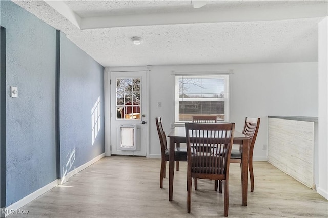 dining room featuring light wood-style floors, baseboards, a textured wall, and a textured ceiling