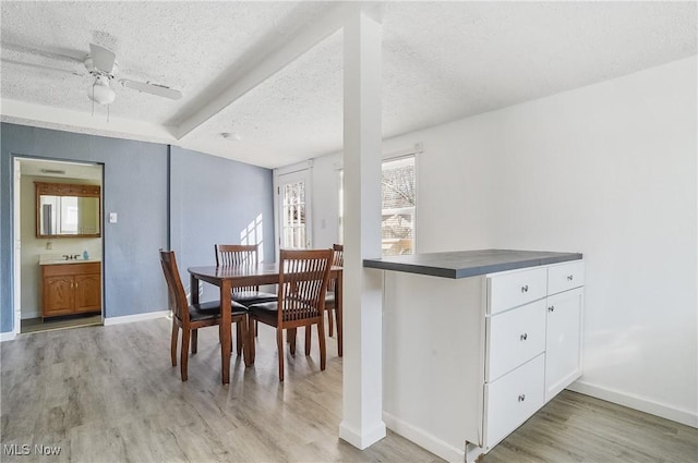 dining space featuring light wood-type flooring, baseboards, a textured ceiling, and a ceiling fan