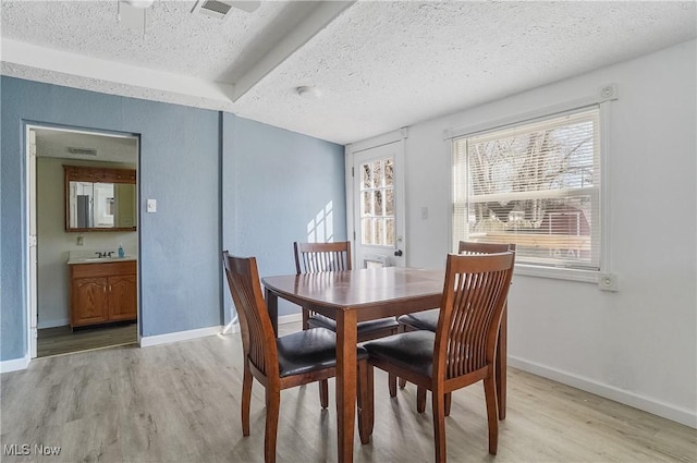 dining space featuring baseboards, a textured ceiling, and light wood-style floors