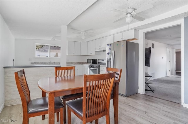 dining area featuring baseboards, a textured ceiling, light wood-style floors, and a ceiling fan