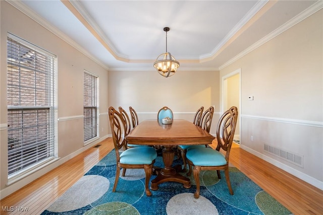 dining space featuring wood finished floors, visible vents, baseboards, an inviting chandelier, and a tray ceiling