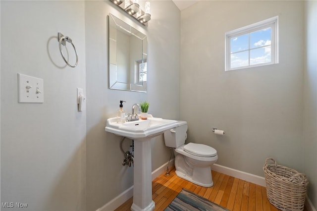 half bath with toilet, baseboards, and hardwood / wood-style floors