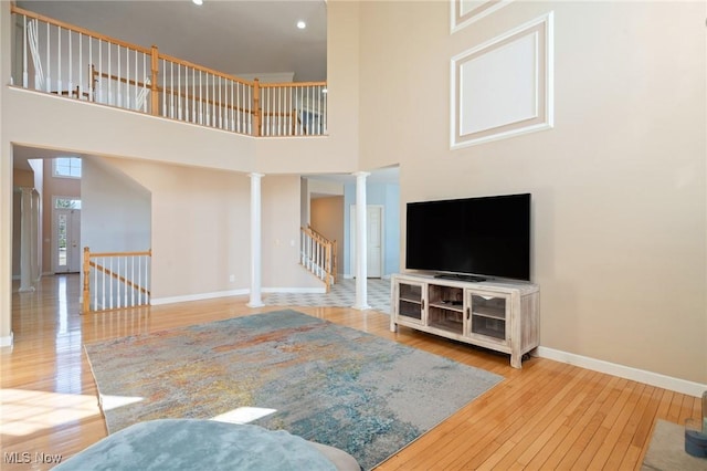 living area with stairway, baseboards, ornate columns, a high ceiling, and wood-type flooring