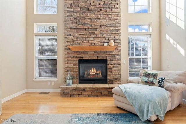 living area with a fireplace, a high ceiling, wood finished floors, and baseboards