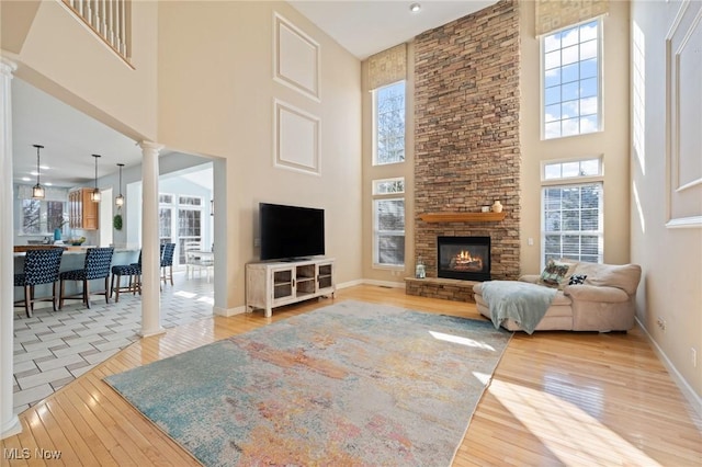 living room with baseboards, decorative columns, a stone fireplace, a towering ceiling, and hardwood / wood-style flooring